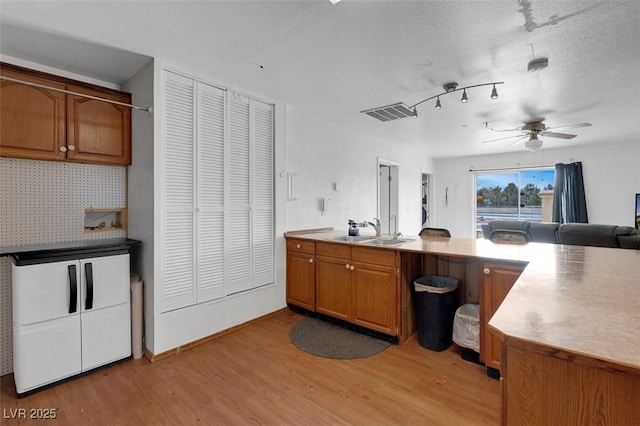 1800 Red Rock Dr, Pahrump, NV 89048 - kitchen with light wood-style floors, brown cabinetry, a peninsula, a ceiling fan, and a sink