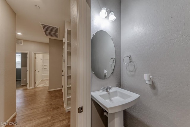 bathroom featuring wood finished floors, baseboards, a sink, and a textured wall