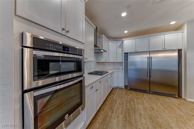 kitchen featuring stainless steel appliances, light countertops, light wood finished floors, tasteful backsplash, and recessed lighting