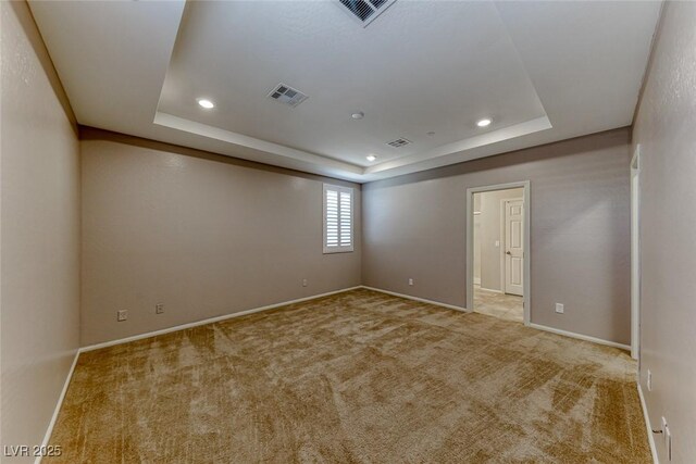 empty room with carpet flooring, a tray ceiling, and visible vents