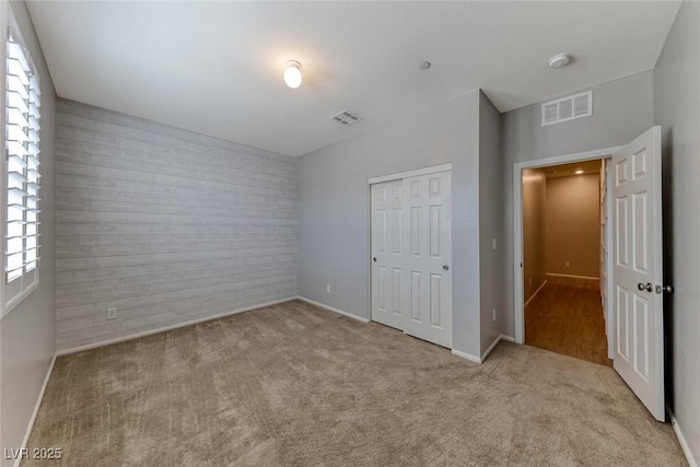unfurnished bedroom featuring an accent wall, carpet floors, a closet, baseboards, and wood walls