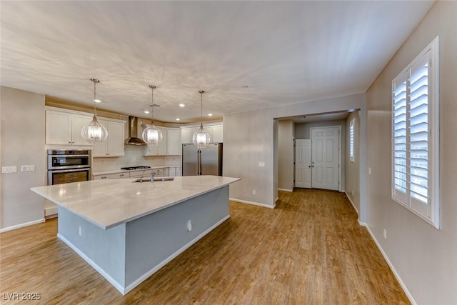kitchen featuring wall chimney exhaust hood, light wood finished floors, white cabinetry, baseboards, and appliances with stainless steel finishes