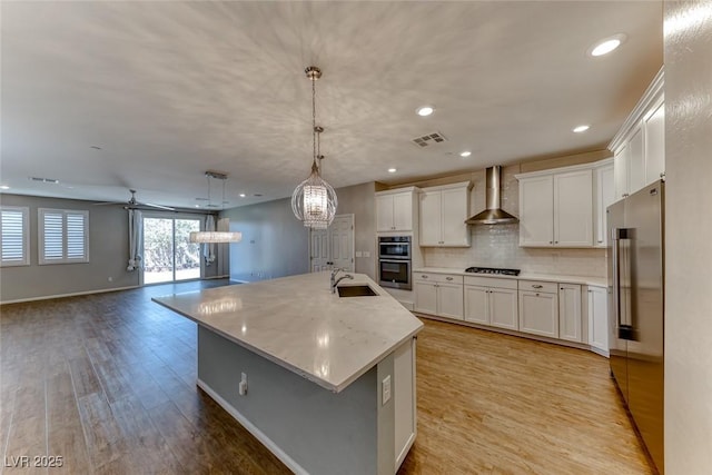 kitchen with light wood-style flooring, a sink, stainless steel appliances, white cabinetry, and wall chimney range hood