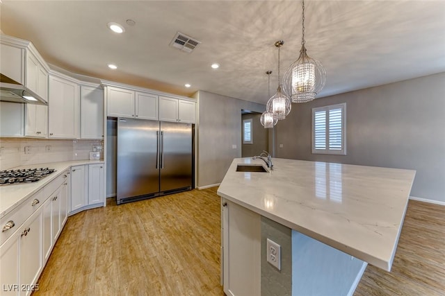 kitchen featuring light wood finished floors, visible vents, a sink, a center island with sink, and appliances with stainless steel finishes