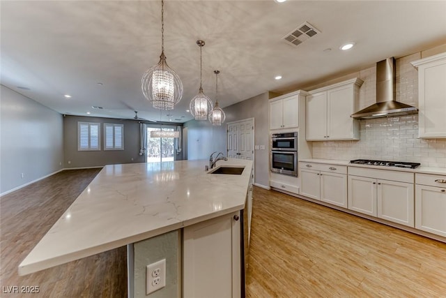 kitchen featuring visible vents, stainless steel double oven, a sink, gas cooktop, and wall chimney exhaust hood