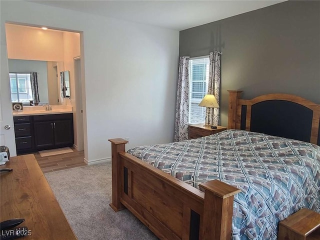 bedroom with a sink, light wood-type flooring, multiple windows, and ensuite bath