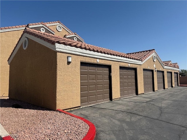 view of property exterior featuring stucco siding, a tiled roof, and community garages