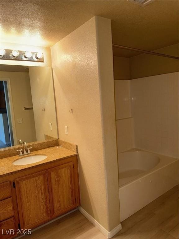 full bath featuring a textured ceiling, wood finished floors, vanity, and shower / bathing tub combination