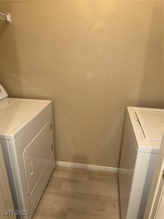 washroom featuring a textured wall, light wood-style floors, washer and clothes dryer, and baseboards