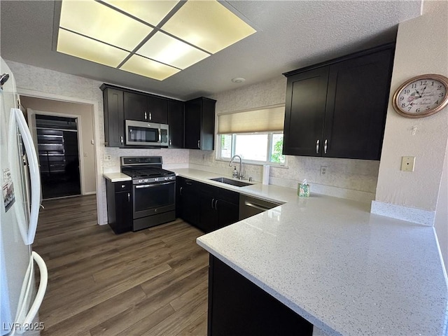 9048 Litchfield Ave, Las Vegas, NV 89134 - kitchen featuring decorative backsplash, a peninsula, dark cabinets, a sink, and appliances with stainless steel finishes