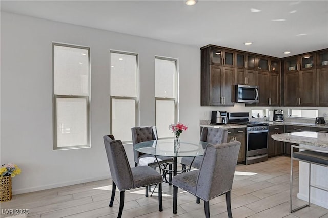 7953 Mountain Lilac St, Las Vegas, NV 89113 - kitchen with glass insert cabinets, appliances with stainless steel finishes, dark brown cabinetry, wood finish floors, and light stone countertops