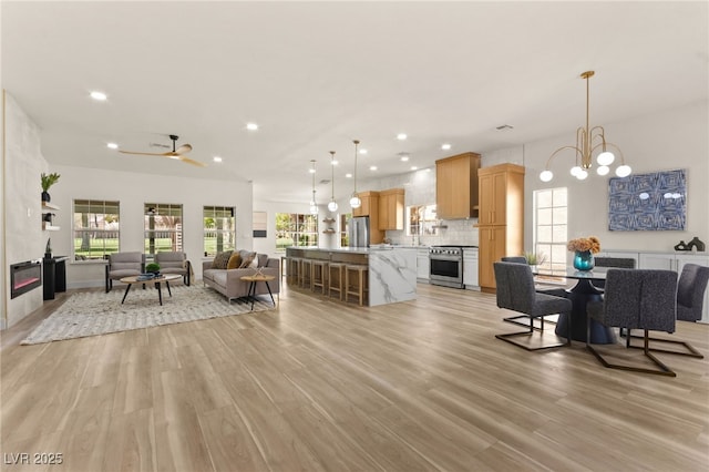 living room with light wood-type flooring, ceiling fan with notable chandelier, and recessed lighting