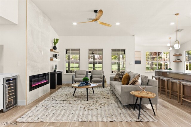 living room featuring a large fireplace, a ceiling fan, visible vents, wine cooler, and wood finished floors
