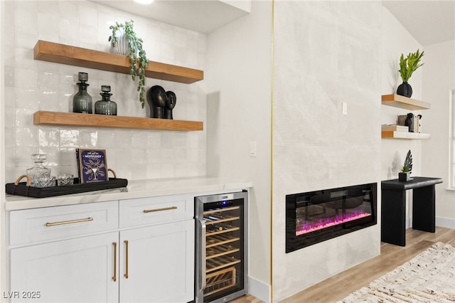 bar with a bar, light wood-type flooring, wine cooler, decorative backsplash, and a glass covered fireplace