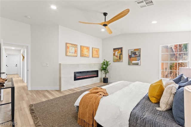 bedroom featuring light wood-style flooring, a glass covered fireplace, visible vents, recessed lighting, and lofted ceiling