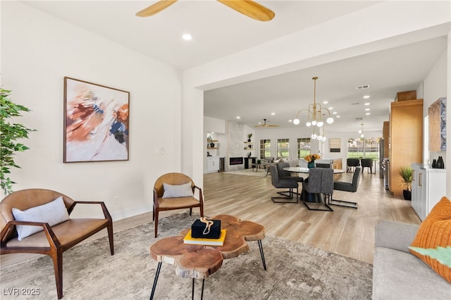 living area with recessed lighting, light wood-style floors, and ceiling fan with notable chandelier