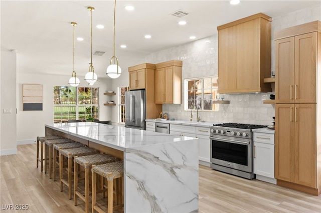 kitchen featuring visible vents, a center island, a sink, a healthy amount of sunlight, and high end appliances