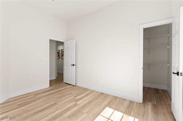 unfurnished bedroom with a walk in closet, light wood-style floors, a closet, and baseboards