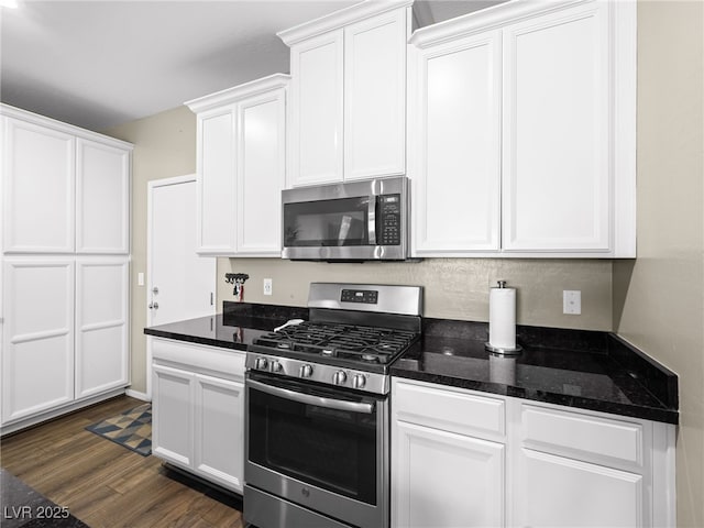 kitchen with dark stone counters, appliances with stainless steel finishes, dark wood-style flooring, and white cabinetry