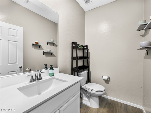 half bathroom featuring vanity, visible vents, toilet, wood finished floors, and baseboards