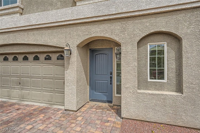 doorway to property with a garage and stucco siding