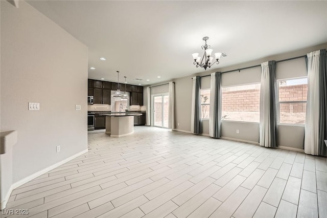 unfurnished living room featuring light wood-style floors, an inviting chandelier, baseboards, and recessed lighting