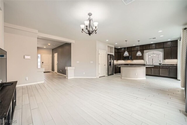 kitchen with dark brown cabinets, open floor plan, appliances with stainless steel finishes, and an inviting chandelier