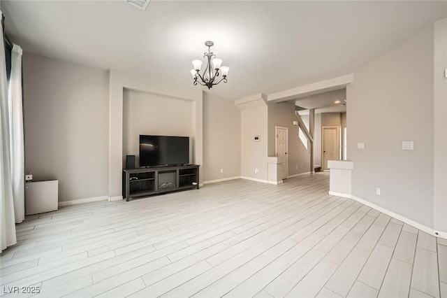 unfurnished living room featuring light wood-style floors, a notable chandelier, and baseboards