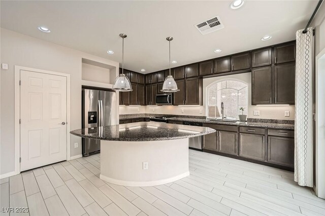 kitchen featuring dark stone countertops, visible vents, a sink, appliances with stainless steel finishes, and dark brown cabinets