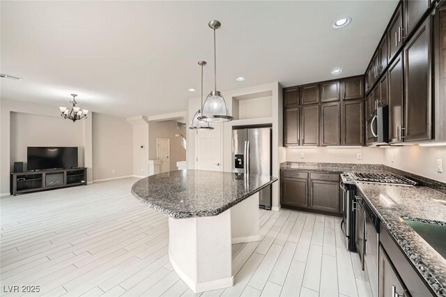 kitchen with recessed lighting, dark brown cabinets, a kitchen island, dark stone counters, and appliances with stainless steel finishes