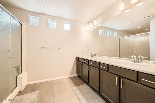 full bath with baseboards, double vanity, a shower stall, visible vents, and a sink