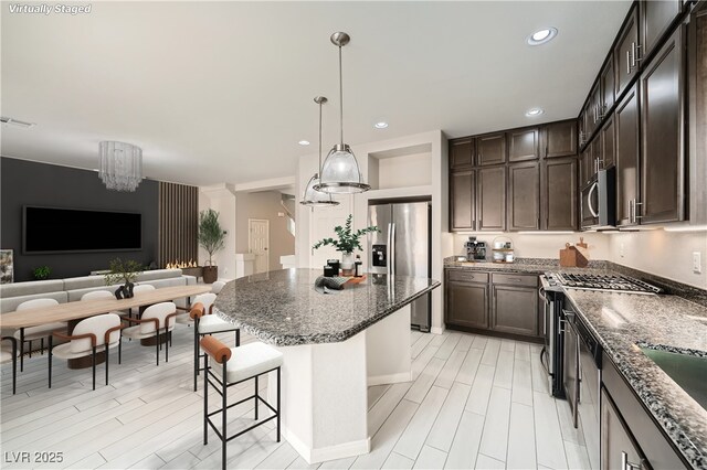 kitchen with dark brown cabinetry, open floor plan, a kitchen island, dark stone counters, and stainless steel appliances