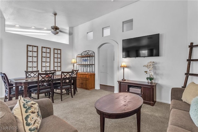 living area featuring light colored carpet, a ceiling fan, arched walkways, and a high ceiling