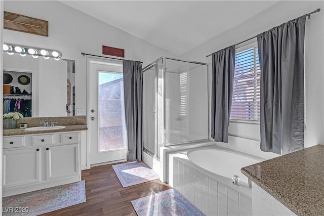 full bath featuring vaulted ceiling, wood finished floors, vanity, a garden tub, and a stall shower