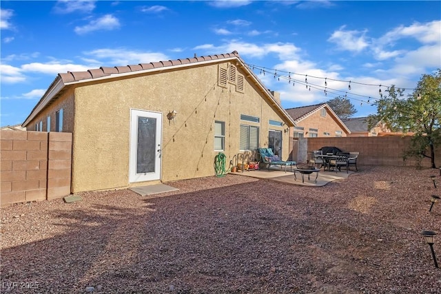 rear view of house with a patio, a fenced backyard, a fire pit, and stucco siding