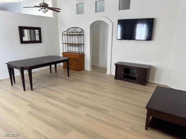 living area with arched walkways, a ceiling fan, light wood finished floors, and baseboards