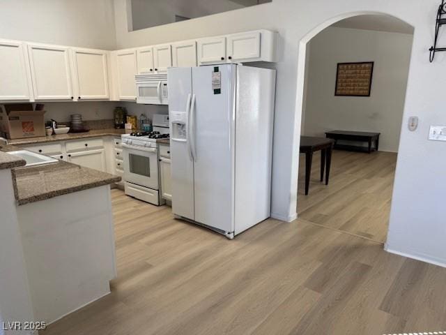 kitchen with white cabinets, a sink, arched walkways, white appliances, and light wood-style flooring