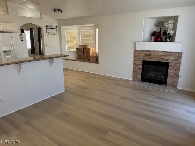 unfurnished living room featuring light wood-style flooring, a stone fireplace, and arched walkways