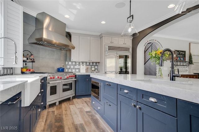 8537 Eureka Heights Ct, Las Vegas, NV 89178 - kitchen with wall chimney exhaust hood, built in appliances, blue cabinets, a sink, and ornamental molding