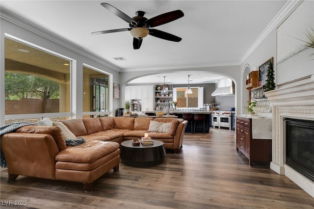 8537 Eureka Heights Ct, Las Vegas, NV 89178 - living room featuring arched walkways, a glass covered fireplace, dark wood-style floors, ceiling fan, and ornamental molding