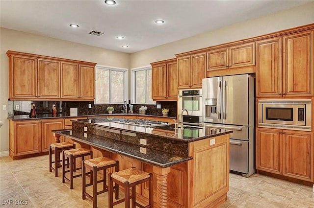 519 Via Garofano Ave, Henderson, NV 89011 - kitchen featuring appliances with stainless steel finishes, brown cabinets, a center island with sink, a breakfast bar area, and backsplash