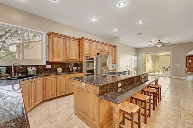 519 Via Garofano Ave, Henderson, NV 89011 - kitchen with appliances with stainless steel finishes, a sink, dark stone counters, a breakfast bar area, and a kitchen island with sink