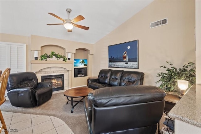 living room with vaulted ceiling, a tiled fireplace, light tile patterned floors, visible vents, and ceiling fan