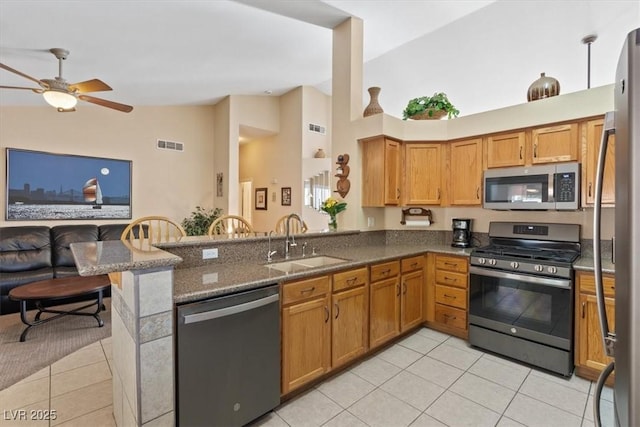 kitchen with light tile patterned floors, dark stone countertops, appliances with stainless steel finishes, a sink, and open floor plan