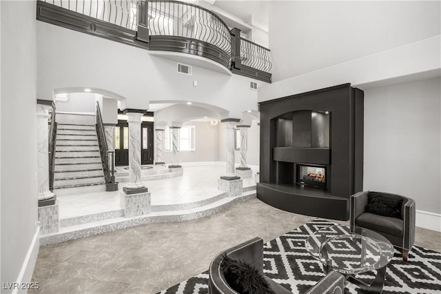 foyer entrance with a towering ceiling, visible vents, arched walkways, baseboards, and decorative columns