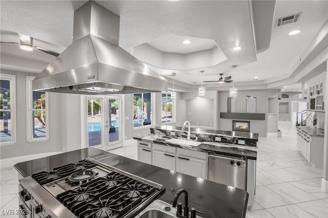 kitchen featuring island exhaust hood, marble finish floor, a raised ceiling, visible vents, and a sink