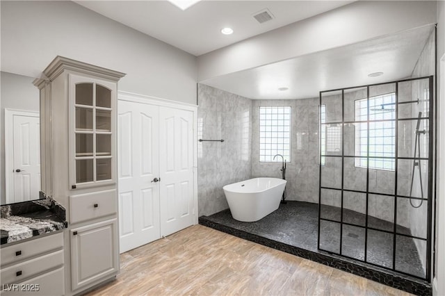 full bath featuring visible vents, vanity, a walk in shower, tile walls, and a soaking tub