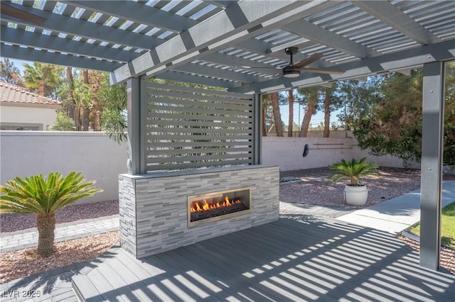view of patio with fence, a pergola, a ceiling fan, and a tiled fireplace