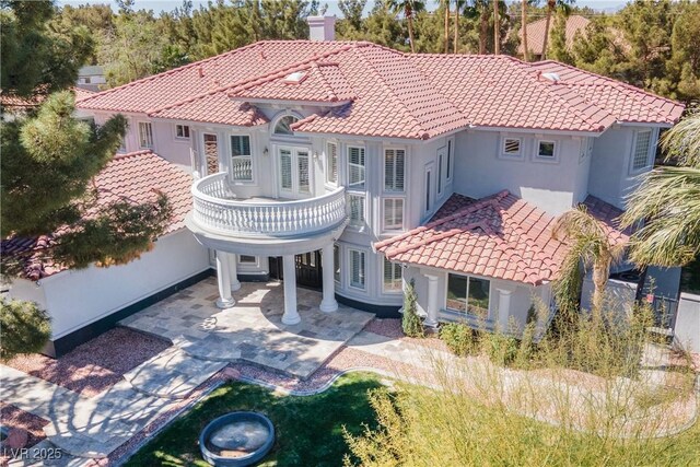 back of house featuring a tile roof, a balcony, a patio area, and stucco siding