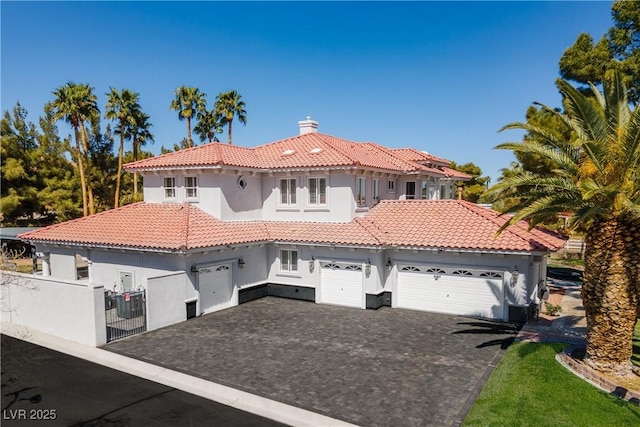 mediterranean / spanish home with a chimney, aphalt driveway, fence, a tiled roof, and stucco siding